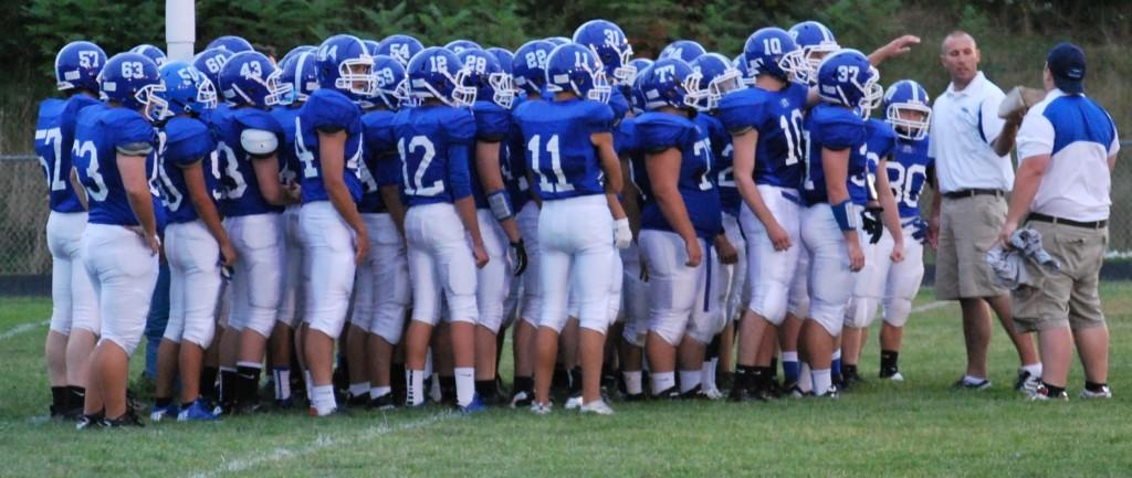 The football team huddled around Coach Bergskaug