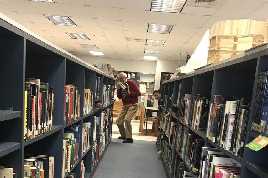 Mike Fox and Christine Heaton pose at the end of the school library aisle. Fox is holding a handful of classic novels while Heaton stands at the end of her beloved bookcase. “What’s the difference between reading a magazine and article posts on Facebook?” said Heaton.